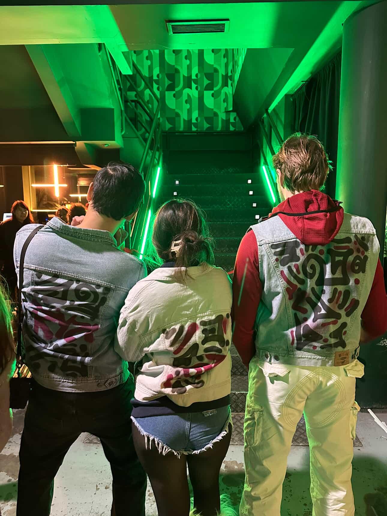 People wearing hand-painted denim jackets on a green-lit staircase